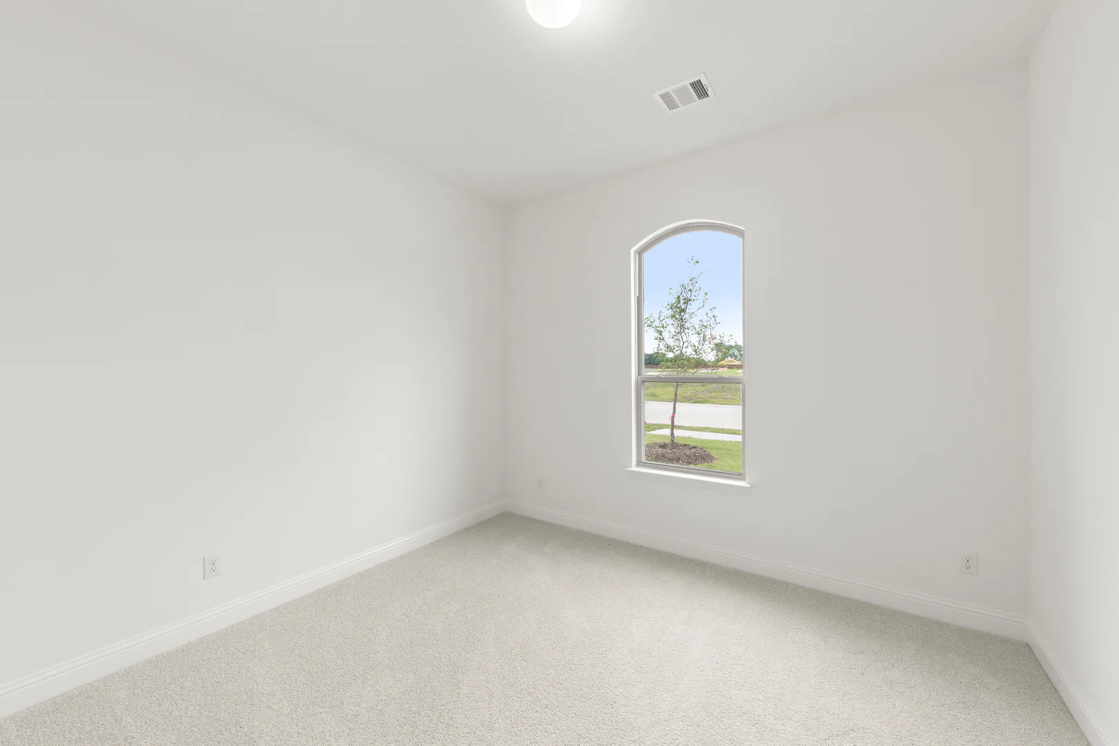 Secondary bedroom with arched window in a modern tudor style home by Kindred Homes