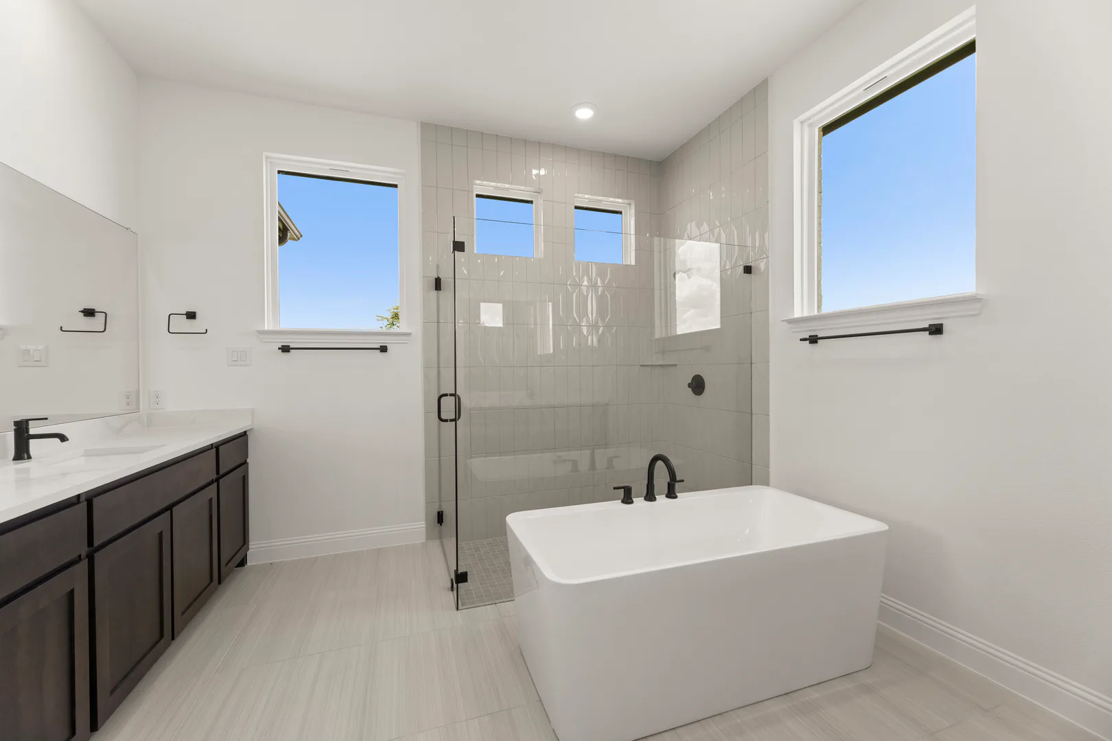 Primary bathroom with freestanding tub, walk-in shower, and separate vanities in a transitional ranch style home by Kindred Homes