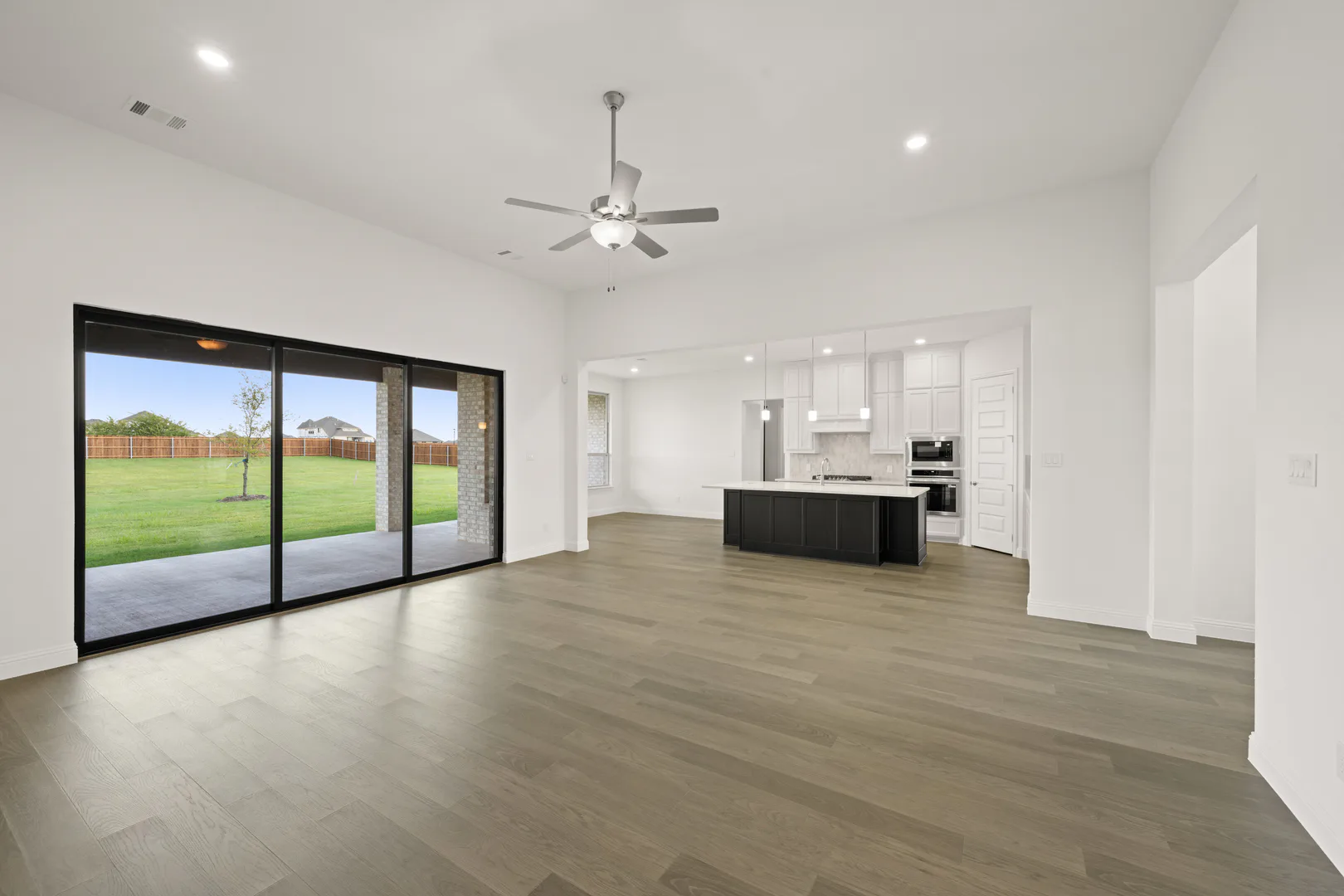 Living room with sliding doors and kitchen in a modern Texas ranch style home by Kindred Homes