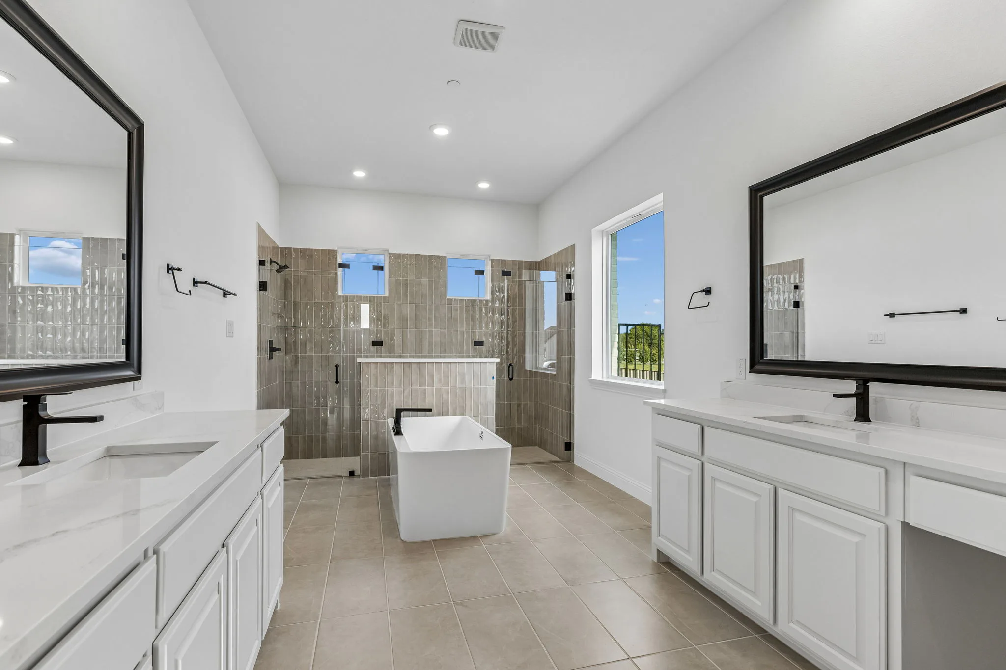 Primary bathroom with dual vanities, freestanding tub, and walk-in shower in a transitional hill country style home by Kindred Homes.