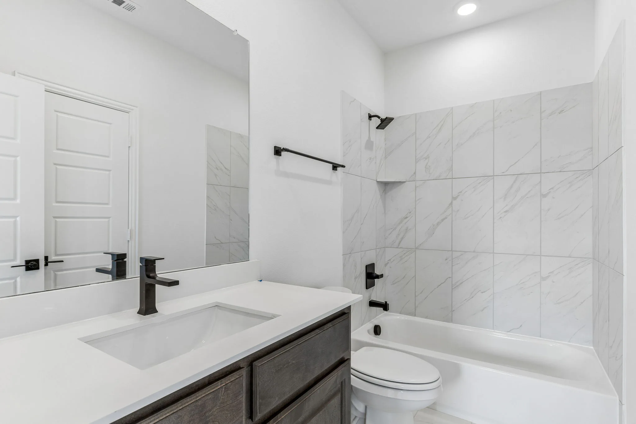 Secondary bathroom with shower/tub combo in a transitional hill country style home by Kindred Homes.